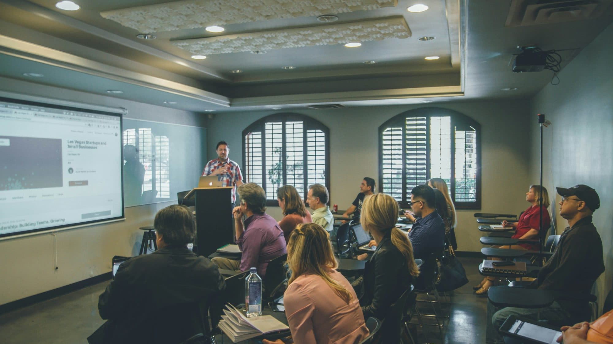 A presenter leads a workshop in front of a large screen while participants follow along