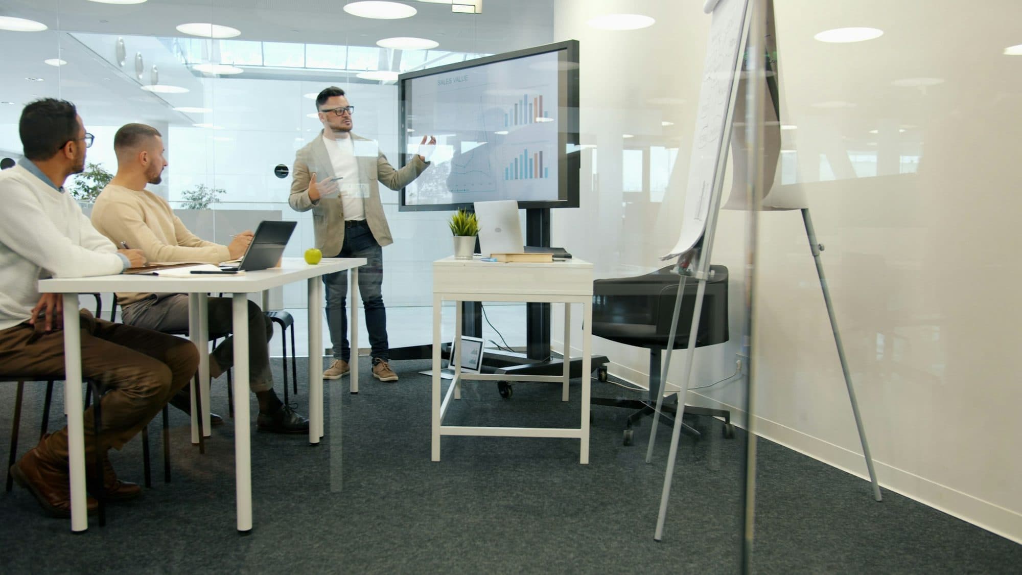 A facilitator presents data on a large screen to a leadership team in a glass meeting room